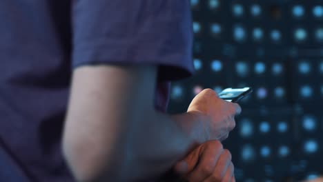 un hombre delgado con una camiseta violeta se sienta en una habitación oscura y utiliza activamente su teléfono inteligente.