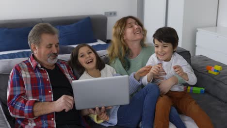 generaciones de familias felices, abuelo con dos nietos y hija sentada en el sofá con una computadora portátil