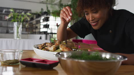 mixed race female chef preparing a dish and smiling in a kitchen