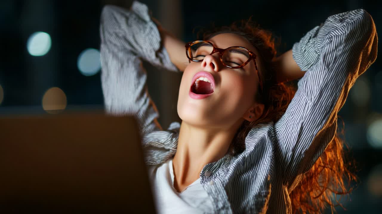 A Young Woman with Glasses Enjoys a Relaxing Moment, Stretching and Yawning While Seated at Her Laptop, Capturing a Sense of Calmness and Contentment in the Nighttime Ambiance