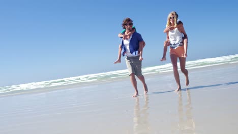 parents giving piggyback ride to their children while running on shore at beach