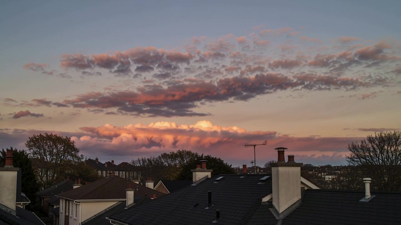 Recording rooftop view showing cloud band shifting color from sunset light over rooftops antenna