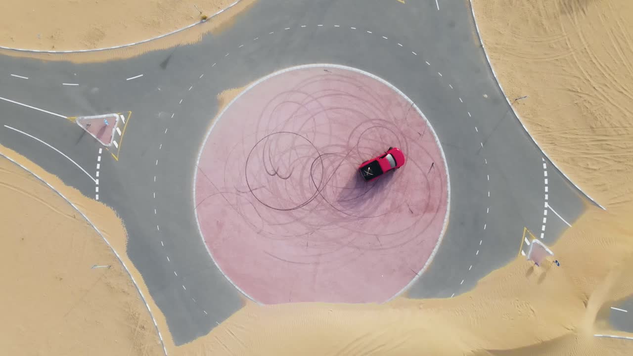 사막 한가운데 있는 원형 교차로에서 표류하는 빨간 트럭의 하향식 드론 보기