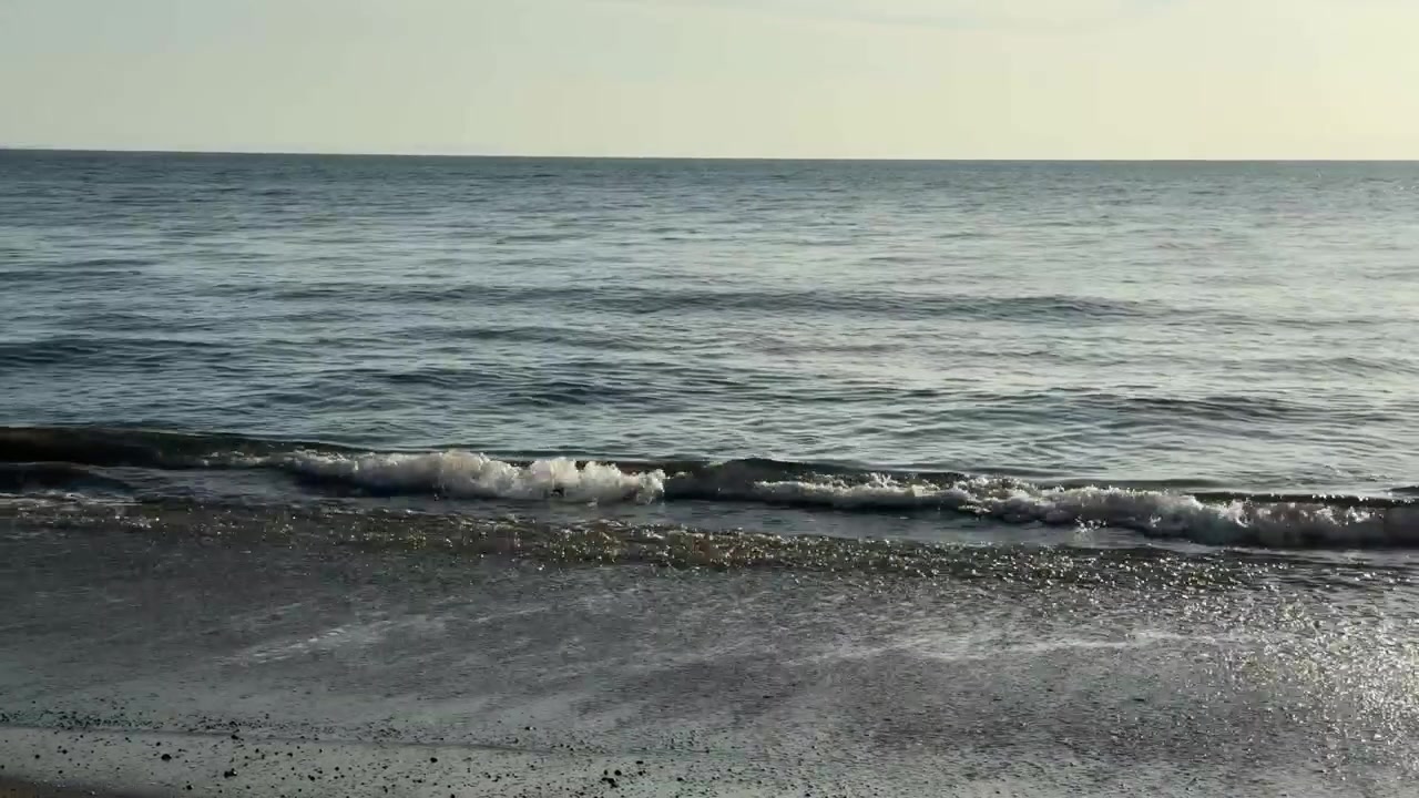Onde marine tranquille che si infrangono su una spiaggia di sabbia scura