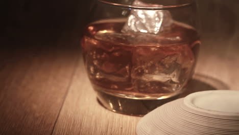 cigar being placed beside tumbler of whiskey on the rocks