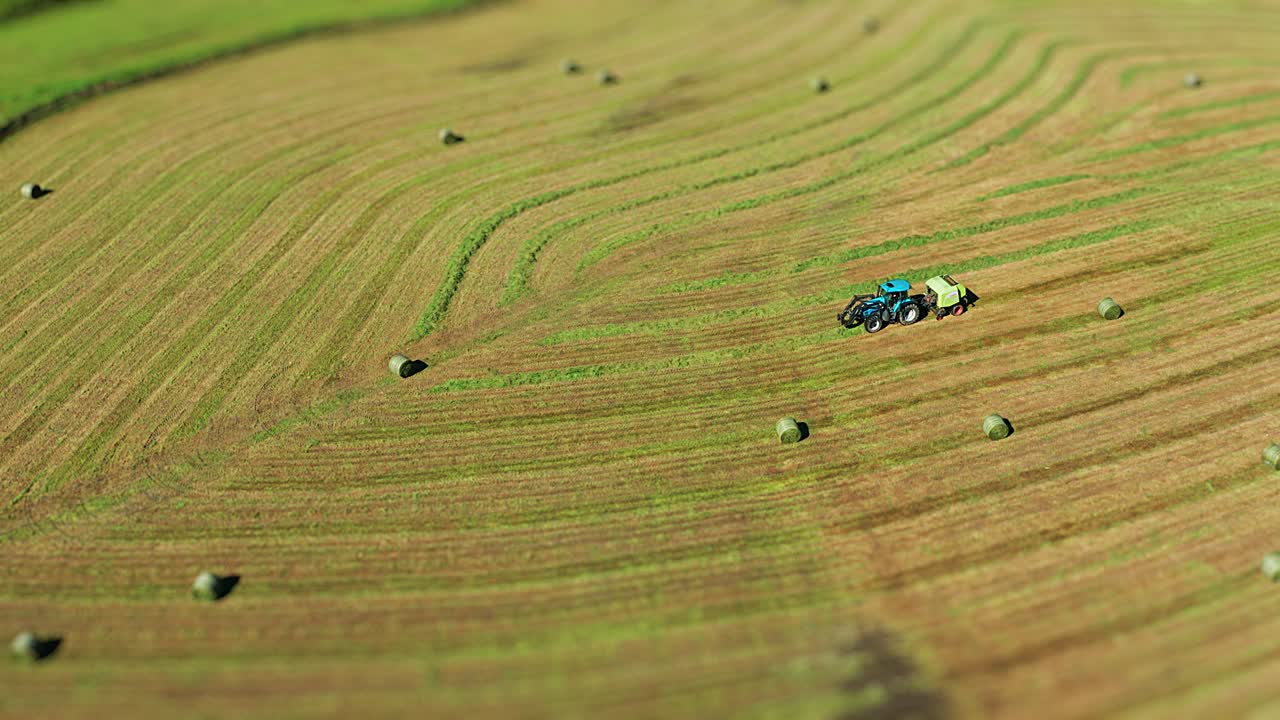 A tractor with a hay bale maker on the freshly mowed field making hay bales