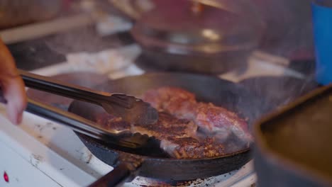 la mano convierte la carne ahumada picante con pinzas de agarre en una antigua cocina de campo, tiro medio de mano