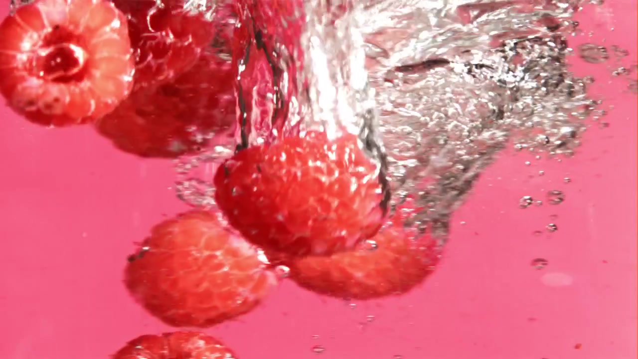 Red Raspberries Falling into Water in Slow Motion on Pink Background