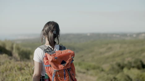 back view of a caucasian girl carrying backpack, walking along the road in mountains