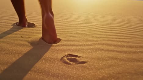 human feet walking barefoot on pristine sandy shoreline during golden sunset, creating meandering footprint trail across soft, warm landscape