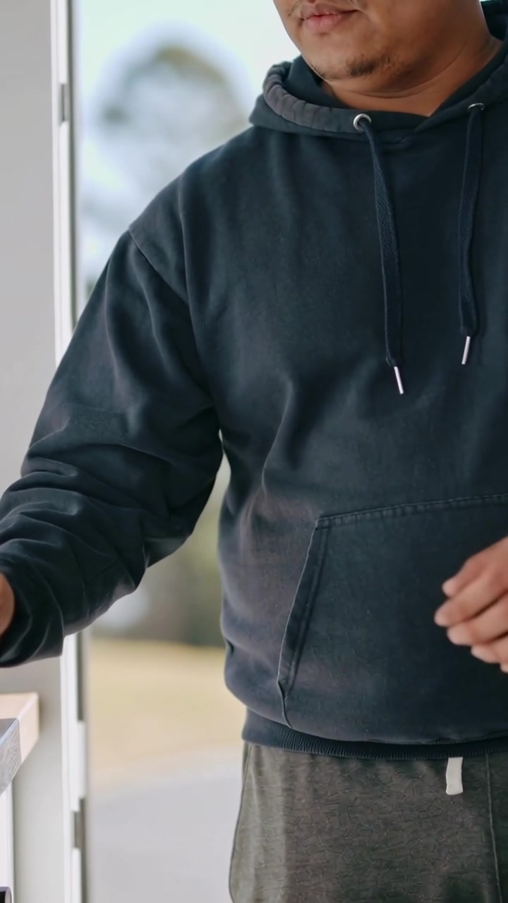 Vertical video: Reaching hooded man lifting cup with sleeve and black lid at doorway counter to sip