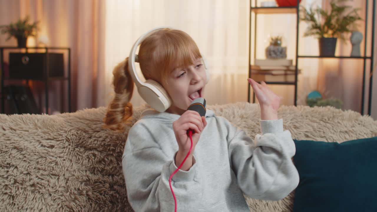 집에서 무선 헤드폰을 입은 젊은 십대 소녀 소파 노래 행위 상상의 무대 유쾌한 에너지