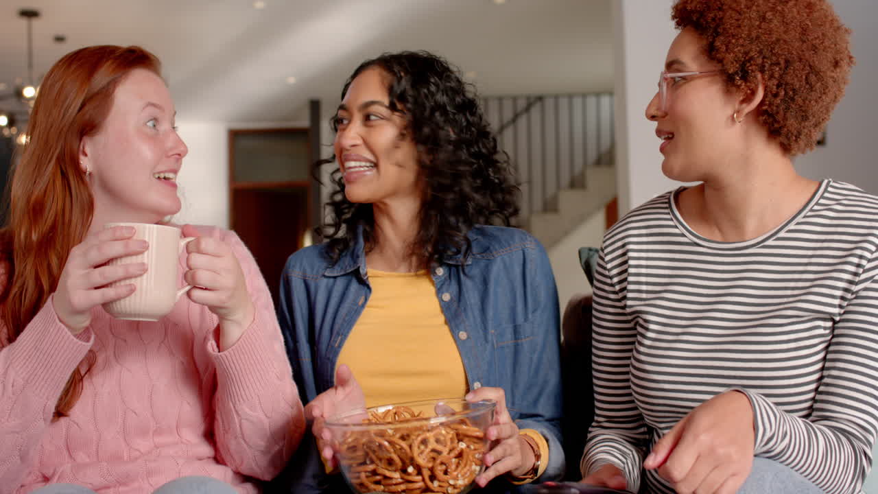 Eating pretzels, diverse female friends chatting and enjoying time together indoors