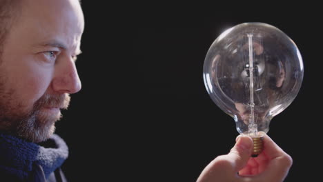 man holding light bulb against black background that loses energy