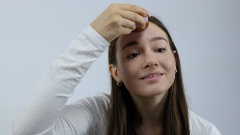 happy and satisfied young caucasian woman applying facial make up with the brush in the morning in front of the mirror white background