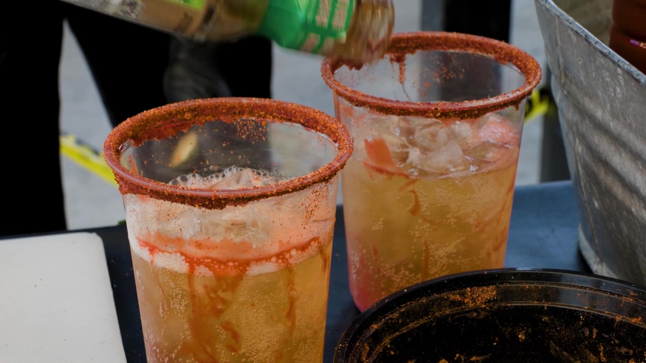 Metraje de preparación de bebidas mostrando a un hombre añadiendo salsa chamoy a una bebida de cerveza durante la preparación de una sabrosa michelada mexicana