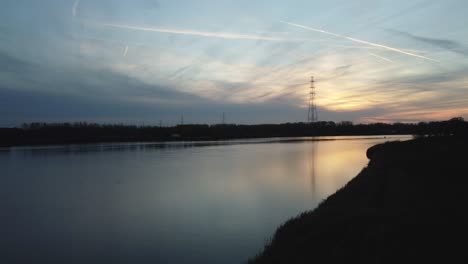 sun setting down over majestic river of scheldt, aerial ascend view