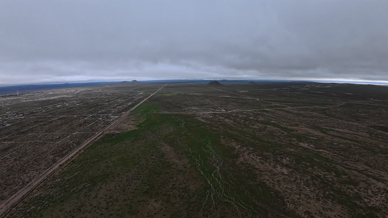 Uma vista aérea calma sobre o Deserto de Mojave após a chuva. A vasta paisagem parece úmida e sutilmente verde, revelando um raro e tranquilo momento no deserto sob um céu nublado