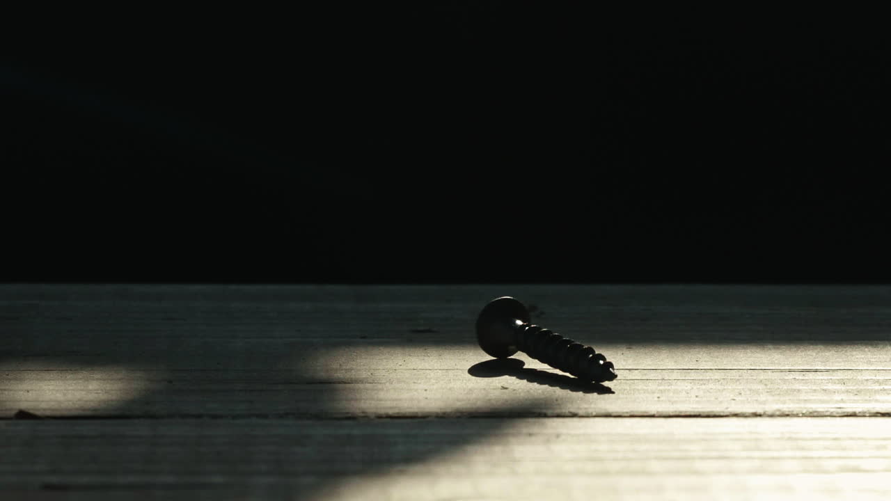 Single wood screw in silhouette on wooden table, Tilt Up to black, Slow Motion