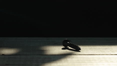 single wood screw in silhouette on wooden table, tilt up to black, slow motion