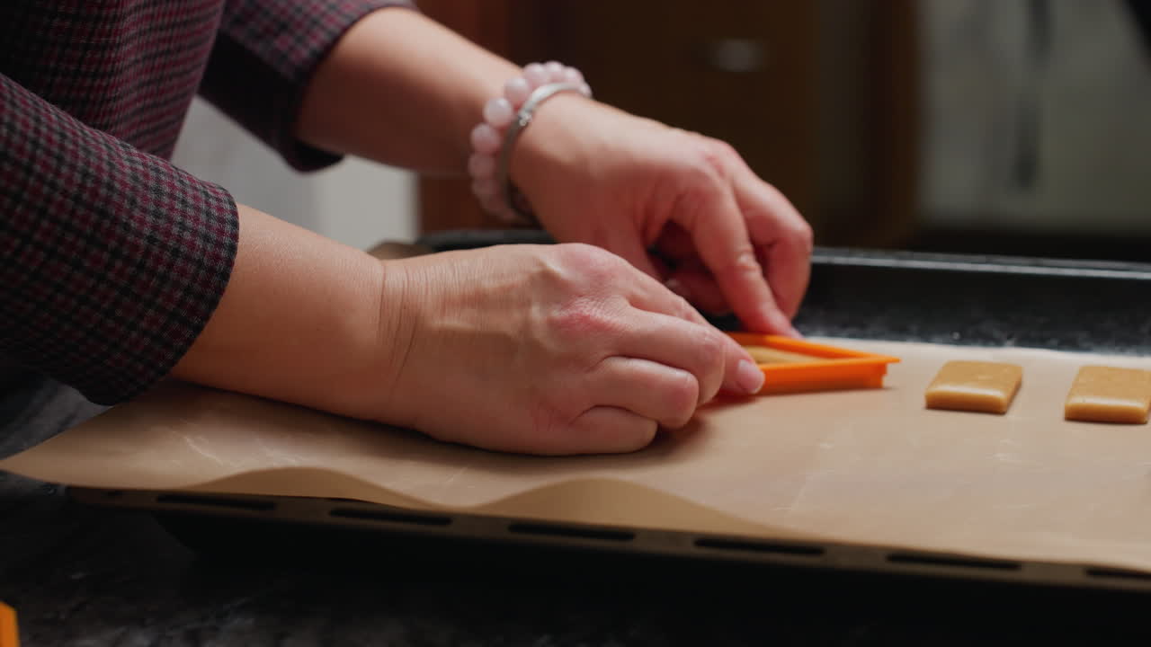 primer plano de un panadero colocando la masa de galletas en forma de papel de pergamino en una bandeja, preparándose para hornear, con rodillo, cortadores de galletas y otras herramientas que rodean la masa en el entorno de la cocina del hogar