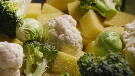 una imagen macro de primer plano de una variedad de verduras frescas cubiertas con condimentos de sal, pimienta y pimentón antes de recibir una llovizna de aceite de oliva