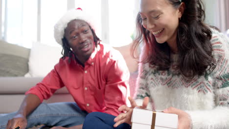 happy diverse couple sitting on floor at home wrapping christmas gifts, slow motion