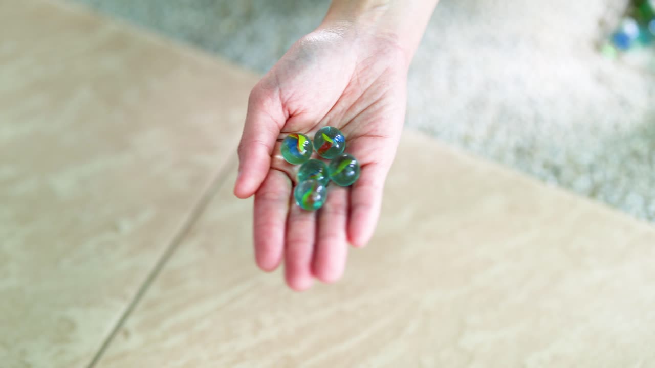 una mano sostiene suavemente los mármoles verdes sobre un piso de azulejos con luz natural, creando una atmósfera serena y enfocada