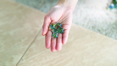 una mano sostiene suavemente los mármoles verdes sobre un piso de azulejos con luz natural, creando una atmósfera serena y enfocada
