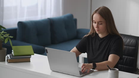 Die-Junge-SEO-Spezialistin-Arbeitet-Von-Zu-Hause-Aus-Und-Tippt-Auf-Der-Tastatur-Eines-Modernen-Laptops-Und-Sendet-Nachrichten-Per-Internet.-Mittleres-Porträt-Im-Wohnzimmer