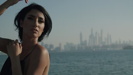 beautiful woman in black dress posing outdoor with foggy dubai marina skyline in background - medium close up shot