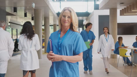 portrait of female doctor wearing scrubs holding patient notes in busy hospital building