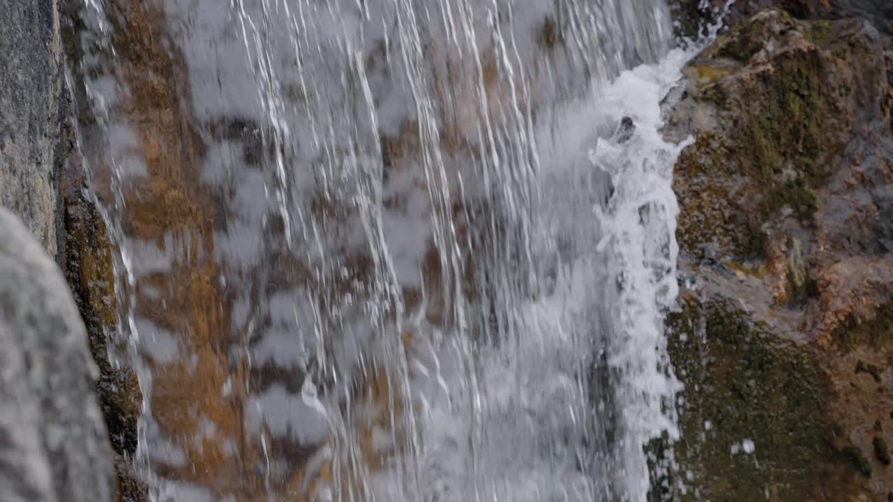 Close up of water cascading over a stone waterfall in a Japanese garden, slow motion pan down