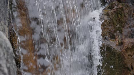 Close-up-of-water-cascading-over-a-stone-waterfall-in-a-Japanese-garden,-slow-motion-pan-down