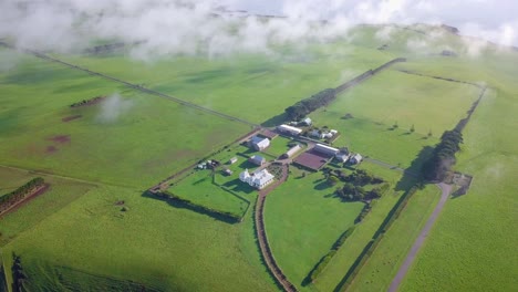 Vuelo-Aéreo-Sobre-Campo-Verde-Y-Granja-Sobre-Las-Nubes-En-Tasmania,-Australia