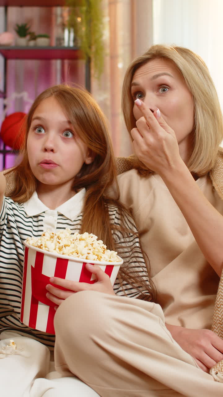 Child girl kid with mother watching cartoon together at home on sofa under warm blanket in room