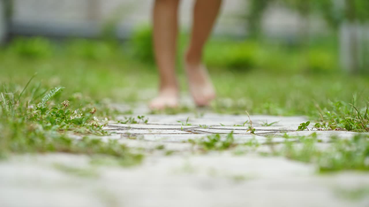 Boy is walking barefoot on the ground in summer. Bare feet of a boy in blue shorts going along the green grass outdoors.