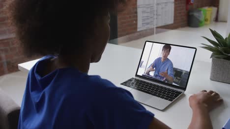 Back-view-of-african-american-woman-having-a-video-call-with-male-colleague-on-laptop-at-office