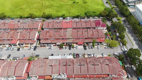 Drone shot of a tightly packed housing area in Klang, Malaysia, showing rows of red rooftops, narrow streets, and parked vehicles in a suburban neighborhood. UHD.