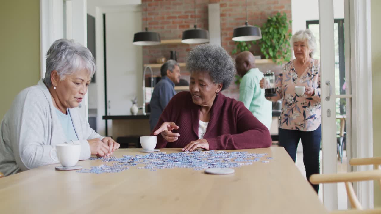 Group of happy diverse senior friends drinking coffee and doing puzzle at home