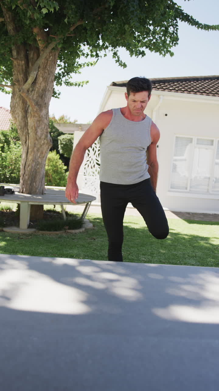 Vertical video of caucasian man doing yoga and stretching in garden, in slow motion