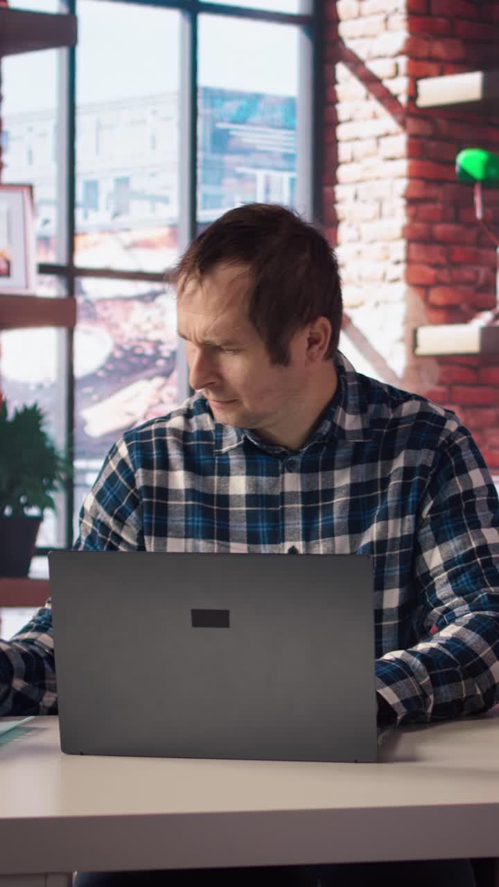 Vertical video Man seated at home office desk using computer, checking emails