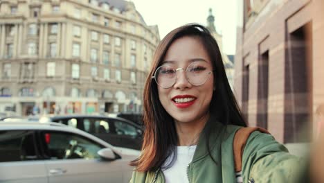 pov of the pretty cheerful young woman in glasses talking to the camera like having videochat through webcam and showing the city center