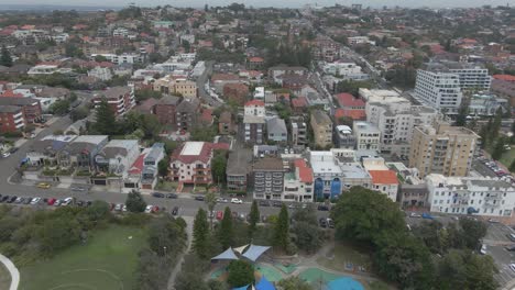 autos estacionados y conduciendo en la calle de la playa pasando por el parque y parque infantil de la reserva de subvenciones - parque infantil conmemorativo de stan windon cerca de la playa de coogee, nsw, australia