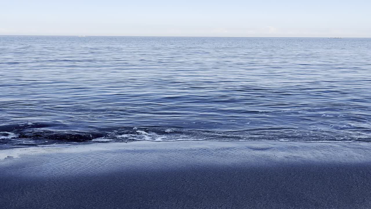Onde calme dell'oceano che lambiscono dolcemente una spiaggia di sabbia scura
