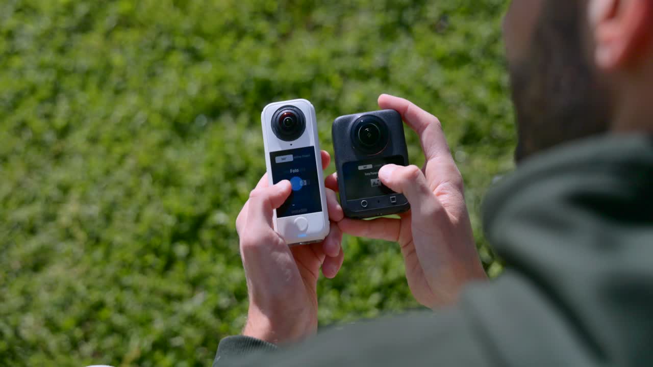 Man holding two 360 action cameras, comparing features for outdoor use