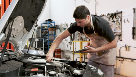 Hispanischer-Männlicher-Automechaniker-Hält-Klemmbrett-In-Der-Hand-Und-Führt-Ölmessstab-Wieder-Ein