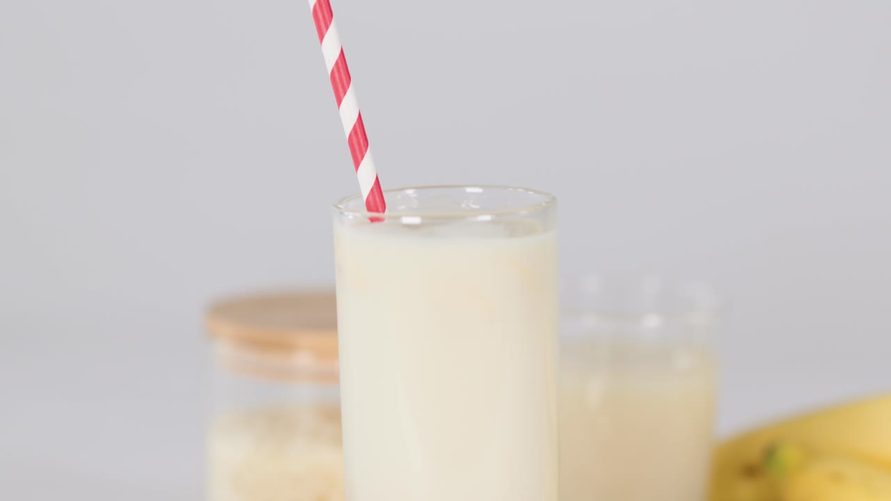 Chia seeds drop into banana milk smoothie glass on wooden table, static closeup shot