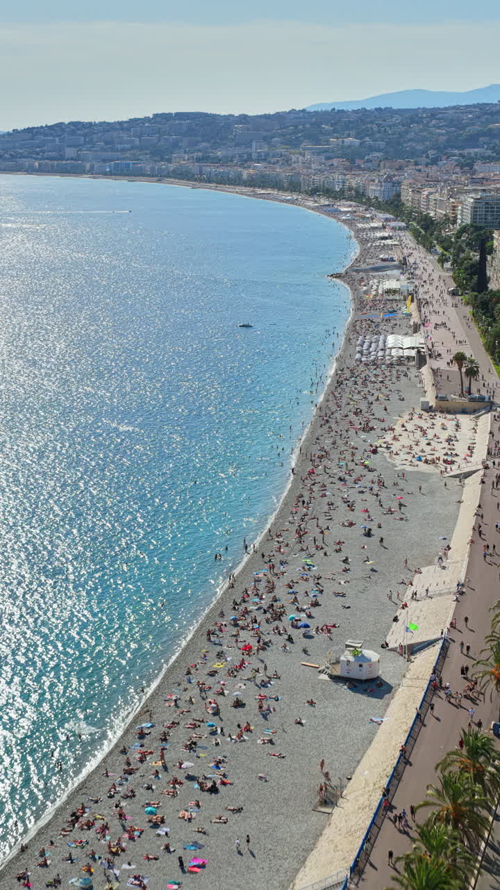 Aerial drone view of the Bay of Angels in Nice, with the Promenade des Anglais, turquoise Mediterranean waters, and parasailers in the distance. Vertical