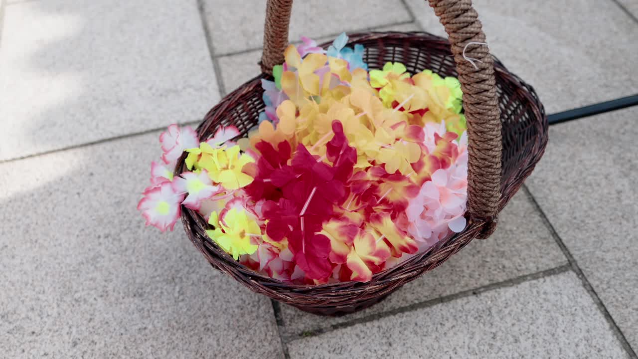bright flower garlands in wicker basket on stone ground at party event